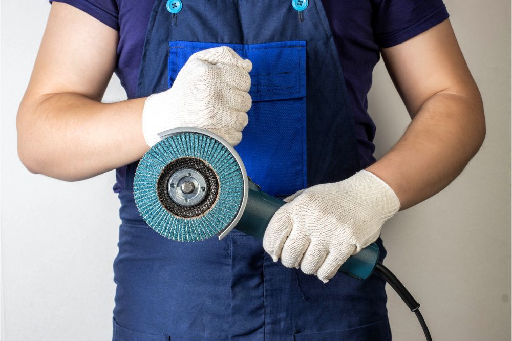 Angle grinder in the hands of a working man against the background of blue overalls.